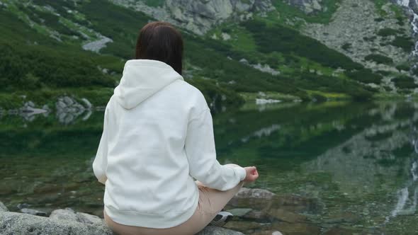 Young Woman Meditating on the Lakeshore with Amazing View on the Waterfall and Mountains. 