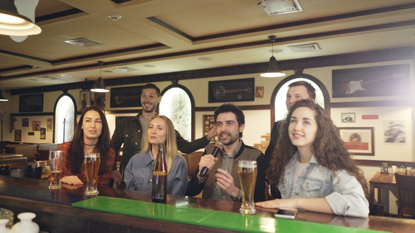 Young Cheerful Friends Singing Together in Karaoke Bar while Sitting at Counter and Having Fun