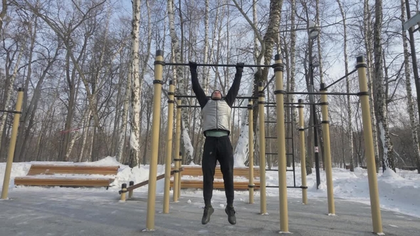 Young Man Doing Pull Up Exercise on Crossbar During Winter Gym Workout