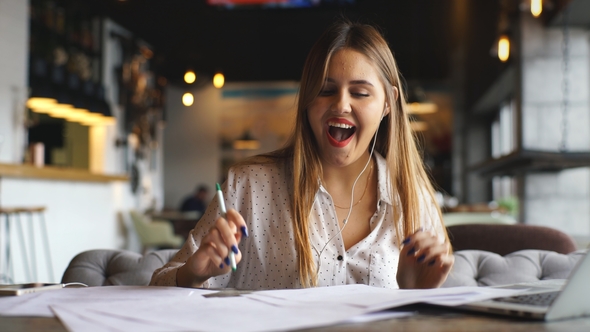 Pretty Young Woman Using Laptop and Listening To Music with Headphones at Workplace