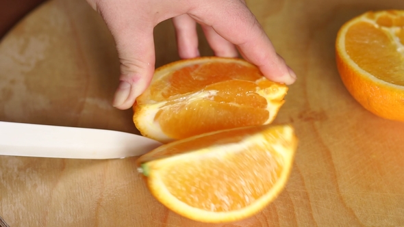 Woman's Hands Cutting Fresh Orange on Kitchen.