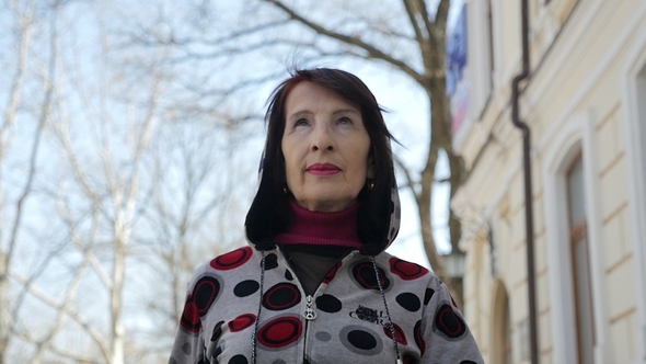 Smart Woman in a Sportive Hoodie Goes Along a Sunny Street in