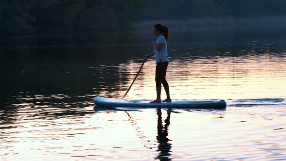 Beautiful Girl Floats Standing on Sup and Rows by Oars at Sunset