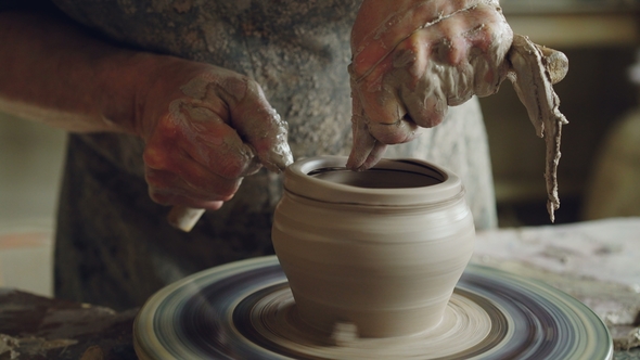 Shot of Half-finished Ceramic Pot Spinning on Throwing Wheel and Hands Cutting Clay 