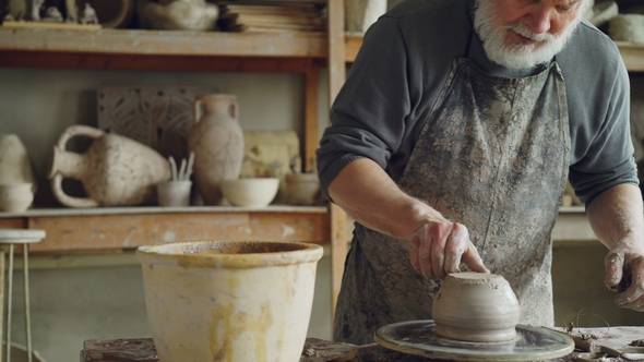 Senior Potter Working at Bottom Part of Ceramic Pot on Spinning Potter's Wheel in Workplace