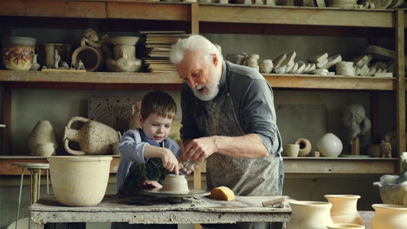 Cute Boy Is Molding Clay on Throwing Wheel While His Caring Grandfather Is Teaching and Helping Him