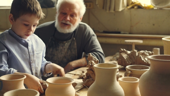 Little Boy Is Playing with Clay Sitting with His Grandparent at Table in Home Pottery Studio