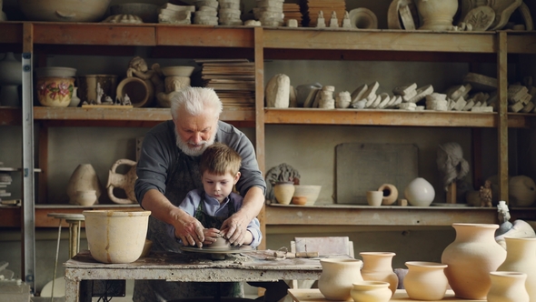 Loving Grandfather Professional Potter Is Teaching His Small Grandchild To Mold Clay on Potter's