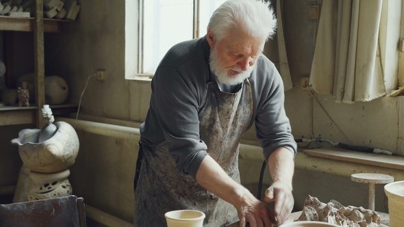 Experienced Male Potter Is Mixing and Kneading Clay on Worktable While Working in Small Workshop