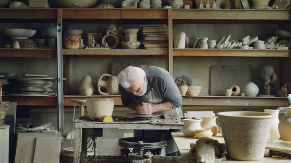 Hardworking Silver-haired Man Working with Clay on Potter's Wheel Shaping Piece of Loam