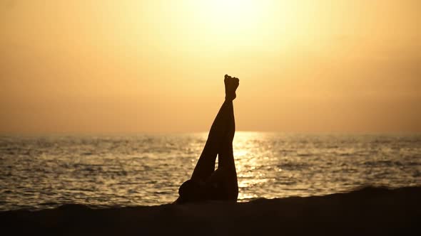 Silhouette of young woman wearing hat relaxing, unwinding at the beach during sunset