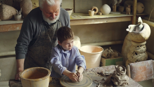 Young Cute Boy Is Making Clay Figure on Throwing Wheel While His Grandfather Experienced Sculptor