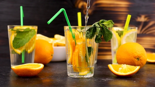 Pouring Water in a Glass with Slices of Oranges