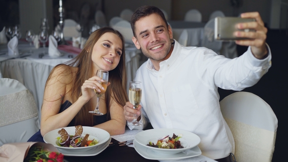 Attractive Loving Couple Is Taking Selfie with Champagne Glasses Using Smartphone While Having