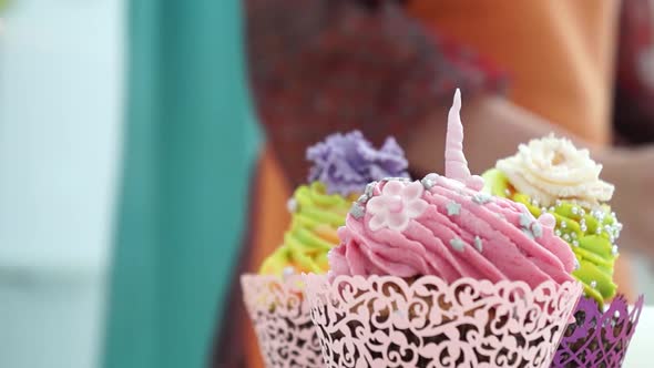 Colorful nicely decorated muffin. Close up of girl baker putting tasty sweet cupcake on the table