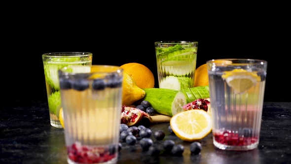 Different Fruits and Berries on a Wooden Board Next To Four Glasses of Detox Water