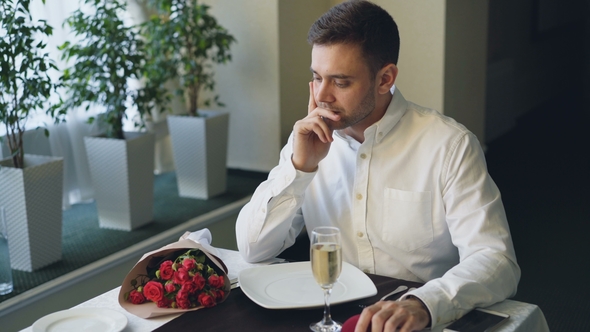 Nervous Man Is Sitting Alone at Table in Restaurant, Drinking Champagne and Waiting