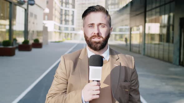 Male TV Reporter with Mic Talking at Camera Outdoors