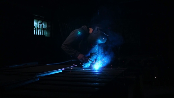 Welder Works in a Mask while Sparks Fly in Different Directions