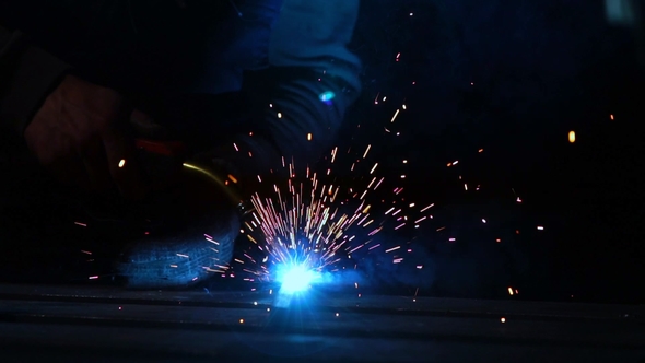 Welder Works in a Mask while Sparks Fly in Different Directions