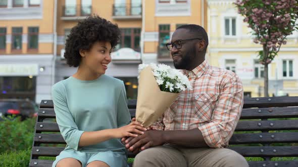 Young Man Giving White Flower Bouquet to Woman Sitting Bench, First Awkward Date