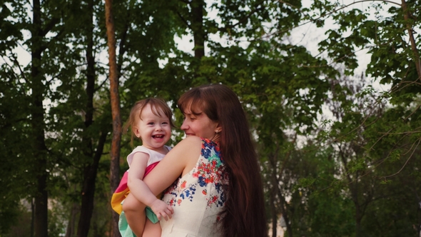 Young Mother Plays in the Park with a Small Baby Laughing and Shaking It in Her Arms