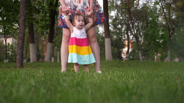 Mom Learns To Walk the Child in the Park on the Green Grass