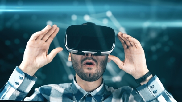 A Young Man with a Beard in Glasses of Virtual Reality on a Technological Background alt