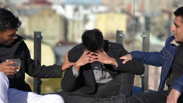 Young Devastated Middle Eastern Man Looking at Camera Sitting with Friends on Sunny Rooftop Outdoors