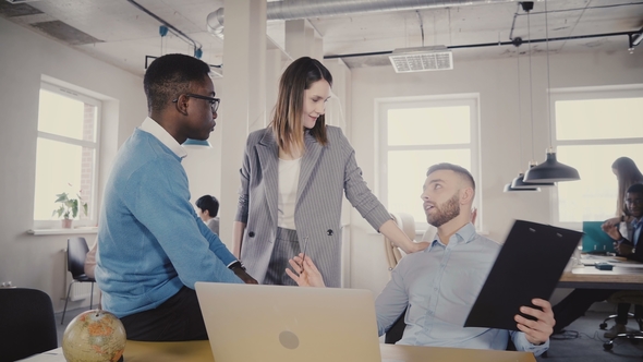 Beautiful Female CEO Discussing Work Process with Young Multiethnic Colleagues, Looks at Laptop