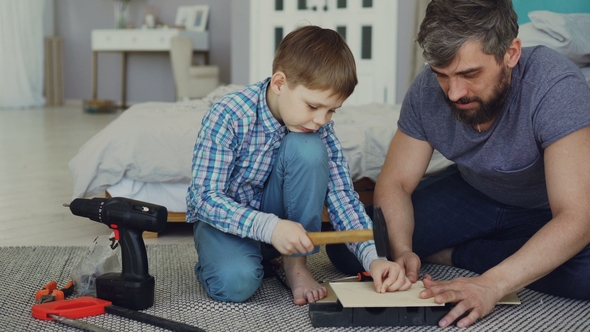 Bearded Father and Young Cute Son Making Birdhouse of Wooden Sheets at Home. Childhood and