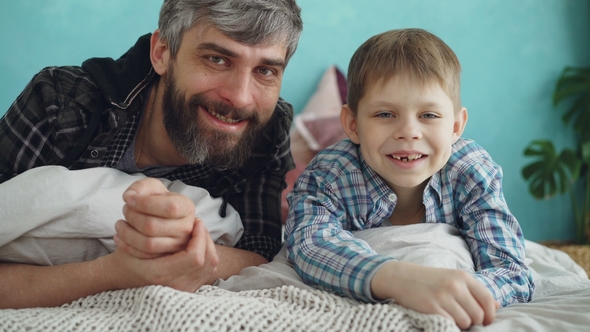 Portrait of Two People Adult Father and Cute Little Son Lying on Bed at Home and Smiling