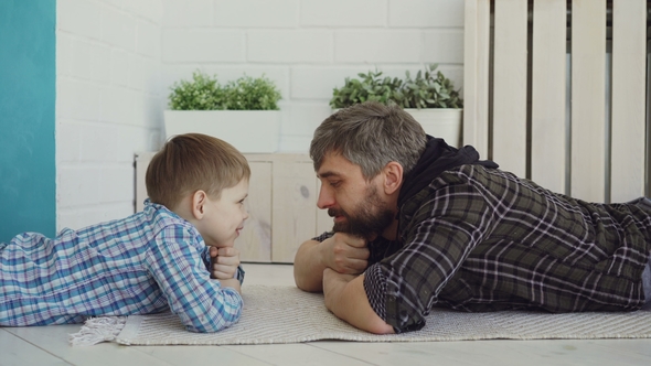 Cute Small Child Is Lying on Floor with His Loving Dad, Looking at Him and Talking