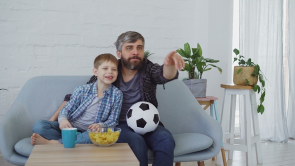 Family Members Father and Son Are Watching Soccer Match on TV at Home, Cheering, Celebrating Victory