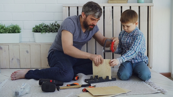 Bearded Father and Little Cute Son Making Birdhouse of Wooden Sheets at Home