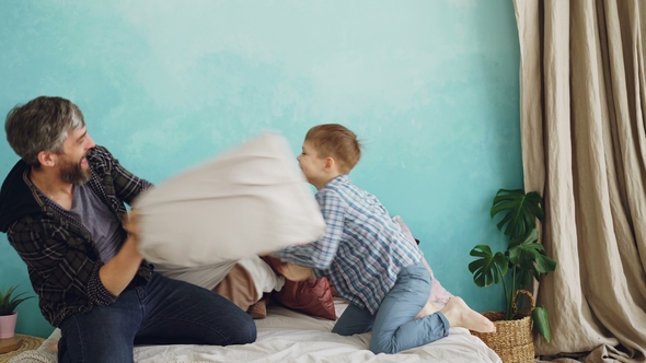 Cheerful Father Adult Bearded Man and Playful Little Son Are Having Fun During Pillow Fight 