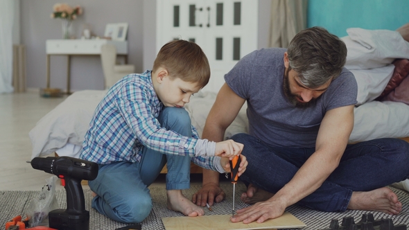Serious Small Boy Concentrated on Putting Screw in Pieces of Wood with Screwdriver