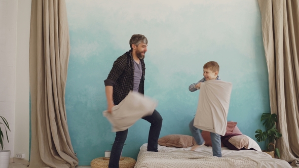 Adorable Playful Boy Is Fighting Pillows, Laughing and Having Fun with His Loving Father. Cheerful
