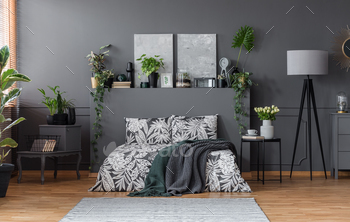 tanding in grey bedroom interior with fresh plants, paintings and lamp