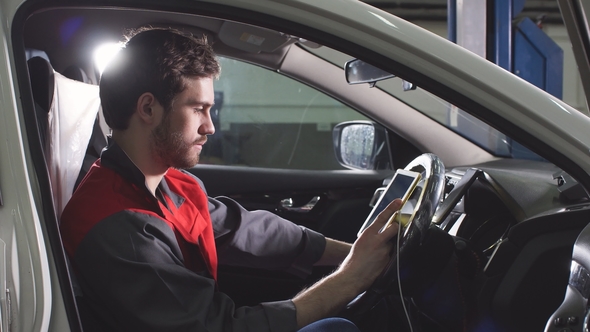 Mechanic Sitting in Car Doing Diagnostics on Digital Tablet.