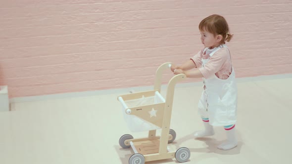 Cute Toddler Baby Girl Pushing A Toy Cart In A Play Zone Cafe. Tracking Shot