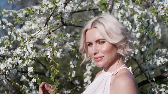 Adorable Young Blonde Girl with Make-up Is Lovely Smiling and Smelling the White Flower in the