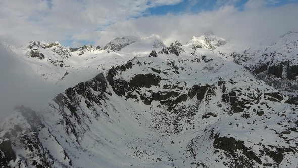 Flying in Clouds Between Snow-capped Mountains