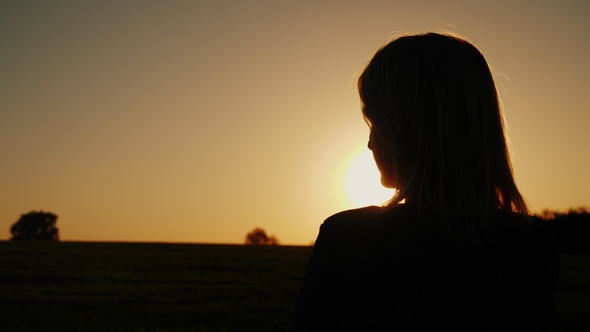 A Thoughtful Woman Looks at the Setting Sun, the Back View. Dreams and Loneliness Concept, Look