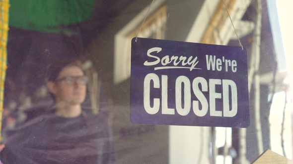 Attractive Male Waiter in Apron Is Changing Doorplate From "Sorry We Are Closed" To "Yes We Are Open