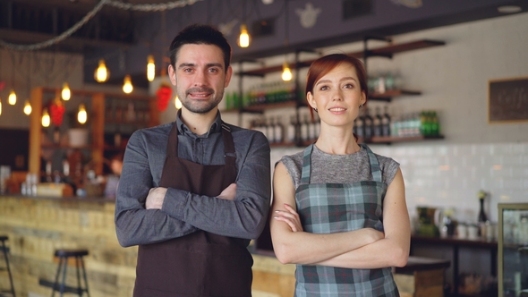 Portrait of Two Cheerful Waiters Standing Inside Cozy Cafe, Smiling and Looking at Camera
