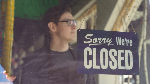 Cheerful Cafe Employee in Apron Is Changing Doorplate From "Sorry We Are Closed" To "Yes We Are Open