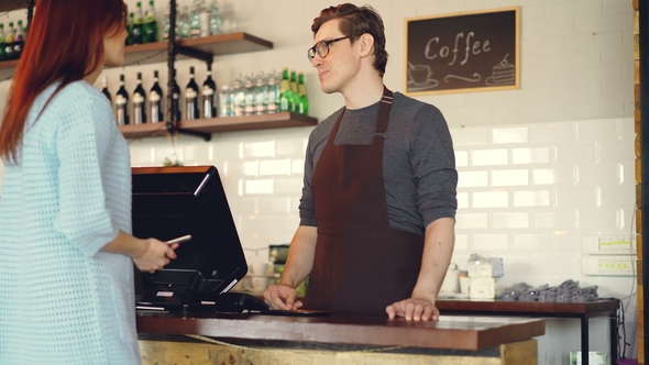 Pretty Young Lady Is Buying Takeaway Coffe in Coffee-shop and Paying with Smartphone Making