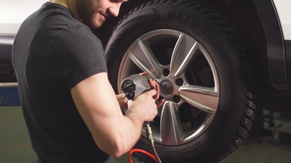 Car Mechanic Changing Car Wheel in Auto Repair Garage.