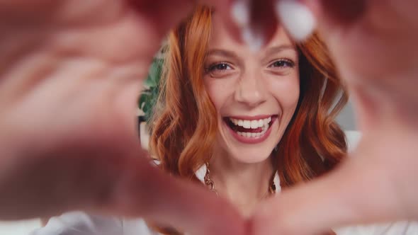 Happy Redhead Woman Making Shape Heart Gesture with Hands on Eve of Valentine